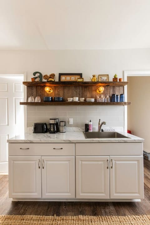 Fully equipped kitchen featuring a refrigerator, sink, stove, toaster, coffee maker, salt and pepper, olive oil, microwave, and essential cooking supplies. A bar table seats two, perfect for shared meals. Handcrafted rustic floating shelves, vintage touch