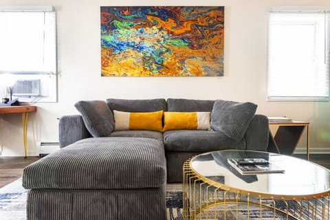 Living room featuring a comfortable couch, a television, and a dining table set over a geometric wool rug. Original modern artwork by Beckerman Photography adds color and creative energy to the vibrant space. 🛋️🎨📺
