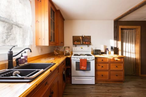 Kitchen Features reclaimed pine wood cabinetry and handmade pine countertops, combining rustic charm with functionality. Fully equipped with a sink, refrigerator, stove, coffee maker, olive oil, salt, pepper, silverware, cookware, dishes, and wine glasses