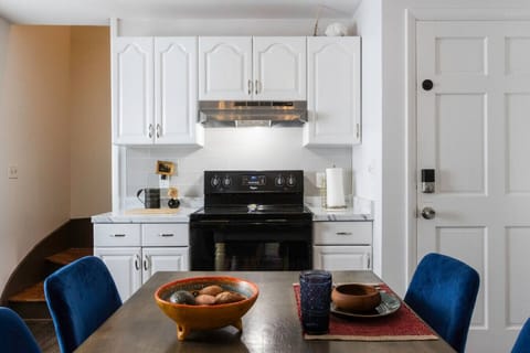 Fully equipped kitchen featuring a refrigerator, sink, stove, microwave, and Instant Pot, along with salt, pepper, olive oil, and essential cooking supplies. A farmhouse table seats four, perfect for shared meals. Handcrafted rustic floating shelves, vint