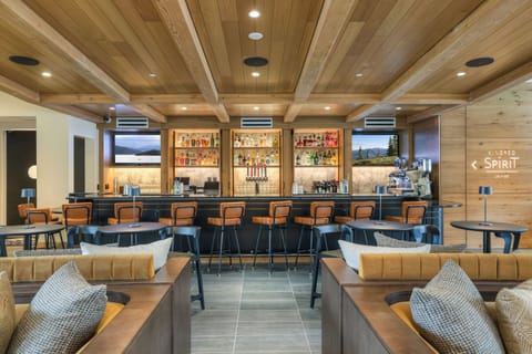 Indoor bar with stools, shelves of bottles, and wooden ceiling.