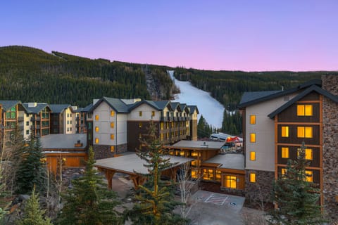Buildings with lit windows, mountains, and ski slopes in background.