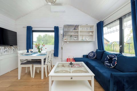 A bright living room with white walls, a blue sofa, and a small dining table. Large windows bring in plenty of natural light.