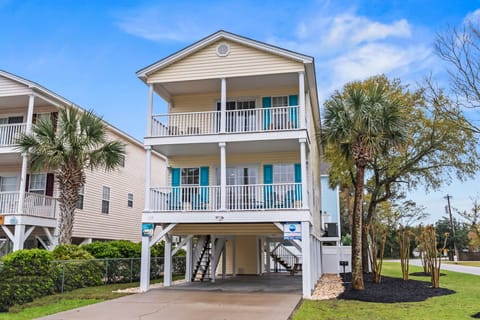 Charming coastal home with double-story balconies and palm trees, featuring covered parking and bright turquoise shutters in a peaceful neighborhood.