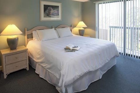 Sink into plush bedding beside sunlit balcony doors.