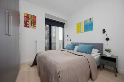 A stylish bedroom corner with a bed and colorful wall art. The room is well-lit, giving it a fresh and airy atmosphere.