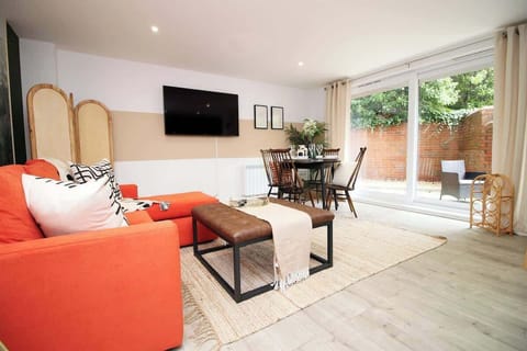 “Bright, stylish open-plan living area with a comfortable sofa bed, large Smart TV, and dining space. Floor-to-ceiling doors open onto a private patio, filling the room with natural light — perfect for relaxing or accommodating extra guests.”