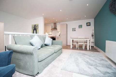 A bright, modern open-plan living space featuring a plush sofa, stylish accent wall and soft lighting. Flowing seamlessly into the dining area and kitchen, it offers a spacious, comfortable setting perfect for relaxing or socialising.