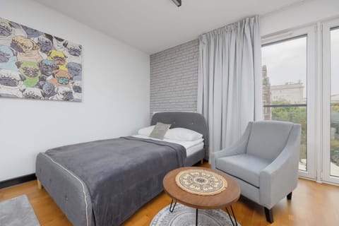 A bright bedroom with a gray bed, side table, and artwork above the headboard