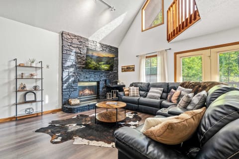 Warm, rustic charm with vaulted ceilings, a stone fireplace, and black leather L-shaped couch.