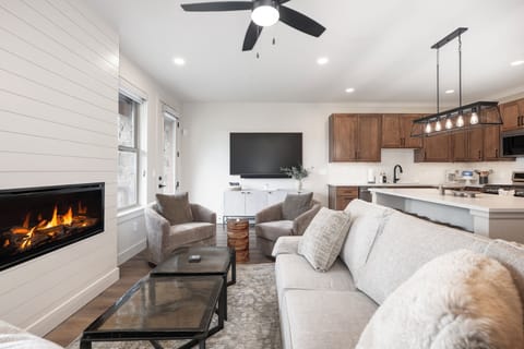 Unwind in your cozy living space where modern elegance meets comfort—crackling fireplace, plush seating, and open kitchen create the perfect retreat.