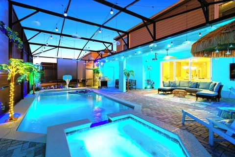 Private screen enclosed pool and spa at night - LED palm trees, string lights, poolside basketball hoop and tiki lounge glowing under the stars.