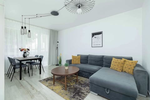 A living and dining space with a dark sofa and small dining table by the window. Warm lighting complements the modern furniture.