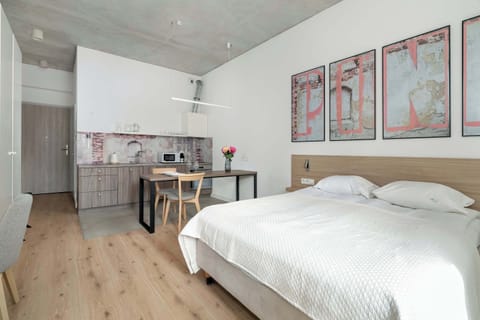 A bright studio with a double bed and a modern kitchenette, featuring wall art above the bed. The space feels open and inviting, with natural light coming through the window.
