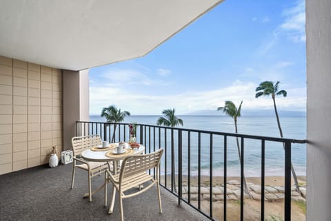 Balcony with small round table and two chairs overlooking the beach with palm trees and ocean, serene and picturesque for relaxation or dining.
