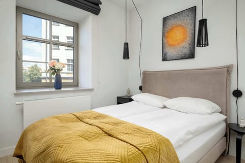 A cozy bedroom area with a golden blanket, large window, and framed artwork on the wall.