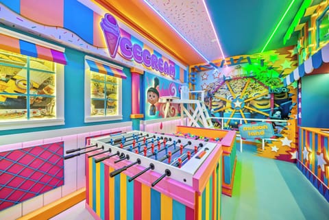 Step into a vibrant playroom filled with color, featuring a lively foosball table and whimsical ice cream-themed decor. The cheerful neon lighting and playful art create an atmosphere that promises fun and relaxation for all ages.