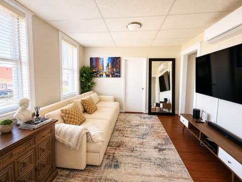 Sunlit lounge with plush sofa, large smart TV, AC, and modern style
