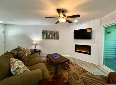 Relax in a cozy living room with a plush sectional, wall-mounted smart TV, and modern electric fireplace. Natural light flows in from the patio doors, creating the perfect spot to unwind after exploring lakes and Clemson.