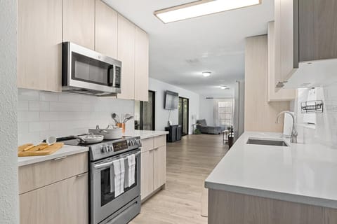 Bright modern kitchen with sleek wood cabinetry, stainless steel appliances, and quartz countertops. Fully equipped for home cooking, seamlessly connected to the open living area for easy entertaining.