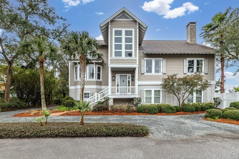 Gray three-story property with palm trees and gravel drive
