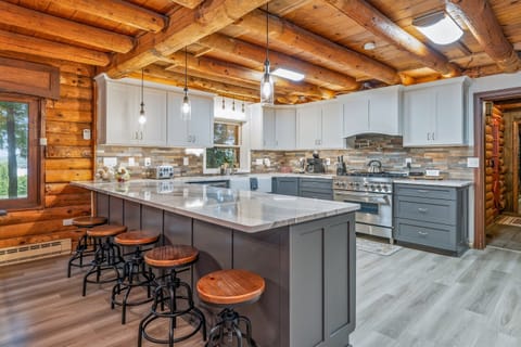 Elegant farmhouse sink, stone backsplash, and premium appliances add modern luxury to this classic log cabin kitchen.