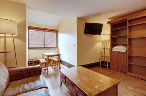 Inviting sitting area with a wall-mounted TV and a quaint dining nook by the window, offering mountain views. Perfect for enjoying meals or relaxing after a day of skiing.