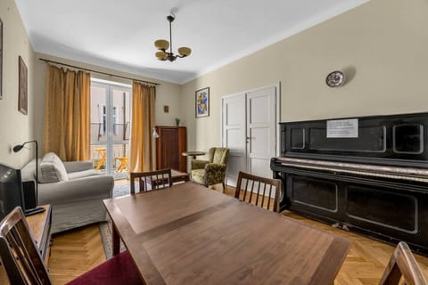 Living Room – Spacious area with sofa, TV, dining table, and even a piano for a touch of charm | Book Now with RENTUJEMY.COM