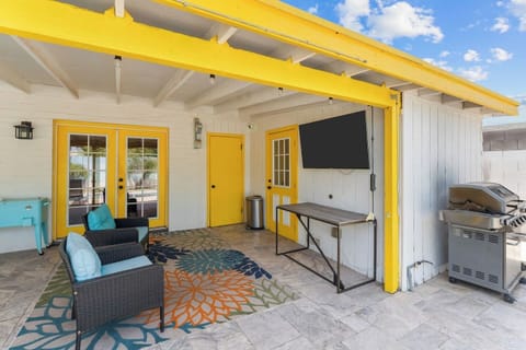 Covered patio with bold yellow accents, outdoor seating, TV, and gas grill.
