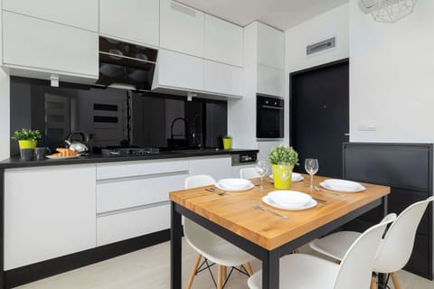 A modern open-plan kitchen with sleek black and white finishes, complemented by a spacious wooden dining table perfect for shared meals.