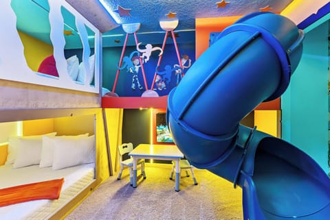 Experience a playful atmosphere in this vibrant children's room, with a fun blue slide leading to cozy sleeping areas. The whimsical art and cheerful desk provide the perfect setting for creative activities and imaginative play.