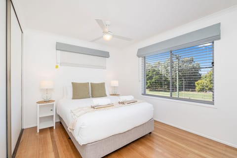 Wake up to natural light and greenery in this peaceful bedroom, complete with soft linen, bedside lamps, and a ceiling fan for added comfort.