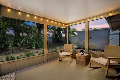 Screened lanai at sunset - string lights, rocking chairs, privacy fence yard.