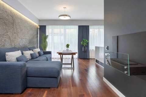 A spacious living room with a gray sofa set, wooden coffee table, and illuminated feature wall. The design combines comfort and elegance.