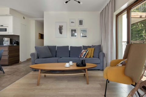 The living room is filled with natural light from large windows, while the comfortable sofa and armchair create a cozy spot to relax after a day full of activities.