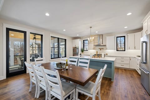 A spacious and modern kitchen and dining area with a large wooden table and access to a beautiful screened in porch with an additional large table and chairs overlooking the lake.