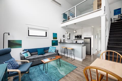 Open-concept living w/ soaring ceilings, loft above & a bright kitchen that flows into a cozy lounge area.