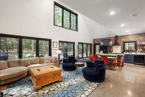 Open-concept living area w/ soaring ceilings, colorful accents, & walls of windows.