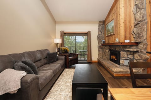 Sink into this plush sectional by your crackling fireplace, where rustic stone meets warm wood and mountain views await beyond your private balcony.
