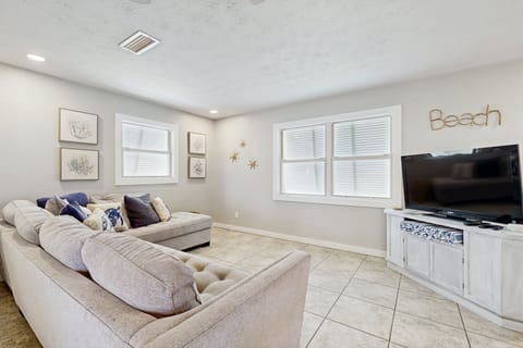 Bright, beach-inspired living room with a cozy sectional, natural light, and a large TV—perfect for relaxing after a day in the sun.