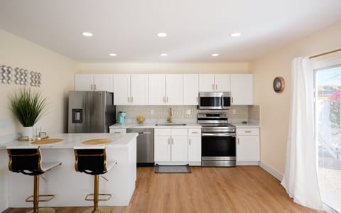 Casita kitchen with white cabinets and countertops, stainless steel appliances, and a kitchen island with breakfast bar seating for two.