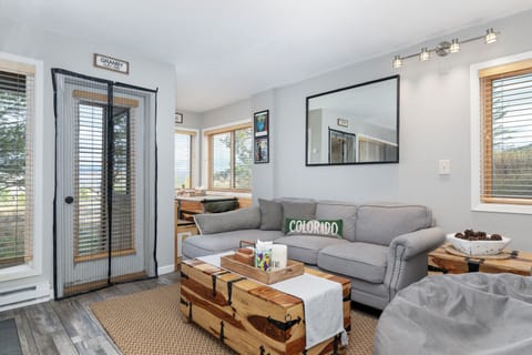Unwind in your bright living space with plush gray seating, natural wood accents, and windows that frame peaceful views.