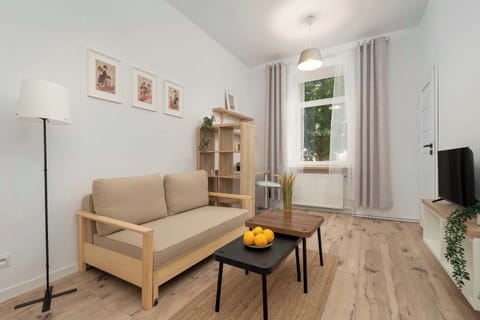 A cozy living room with a beige sofa, wooden coffee table, and a TV stand. Large windows bring in natural daylight.