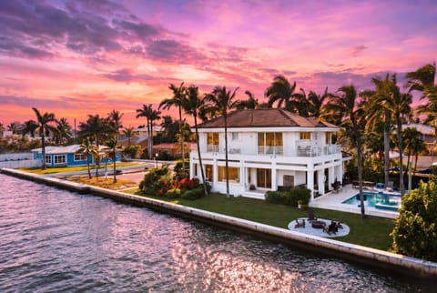 Two-story waterfront property with wrap-around balconies, private swimming pool, and a coastal sunset backdrop