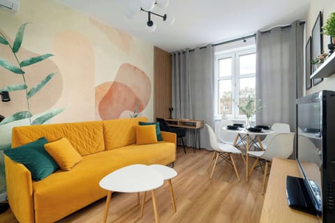 A modern bedroom with a yellow sofa, round coffee table, and large windows with sheer curtains.