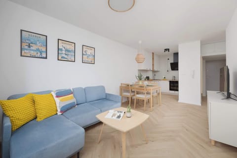 A bright living room featuring a blue sofa with yellow cushions and a coffee table. The space is well-lit and inviting, perfect for relaxing or socializing.