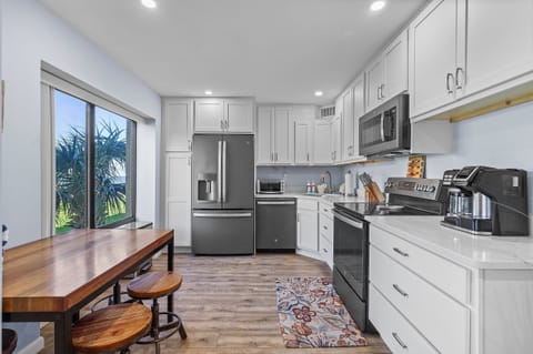 Cook up seaside favorites in this modern, fully equipped kitchen featuring stainless steel appliances, sleek white cabinetry, and a cozy breakfast nook with a view—perfect for your beach getaway.