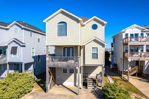 Dawn to Dusk: Front exterior of the home showcasing its elevated coastal design, wide driveway, and spacious three-car parking area.
