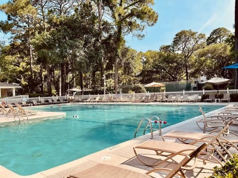  A large, sparkling swimming pool surrounded by plenty of lounge chairs for sunbathing, framed by mature trees for a peaceful atmosphere.