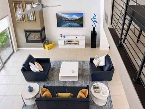 Settle into your spacious living room, where plush seating surrounds a sleek coffee table. Enjoy the warmth of the fireplace, entertain with the large TV, and admire natural light streaming through windows overlooking lush greenery.
